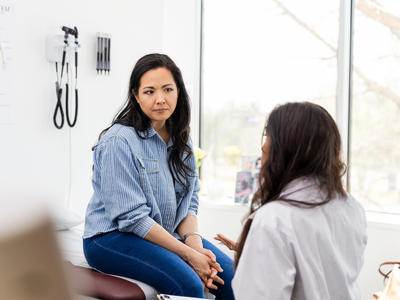 A middle-aged women sitting in a doctor's office speaking with the doctor.